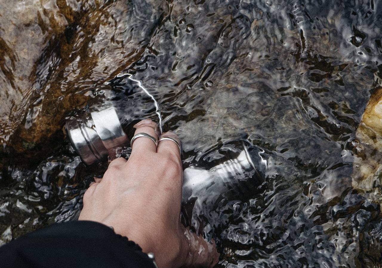Турист набирает воду из ручья в металлическую флягу